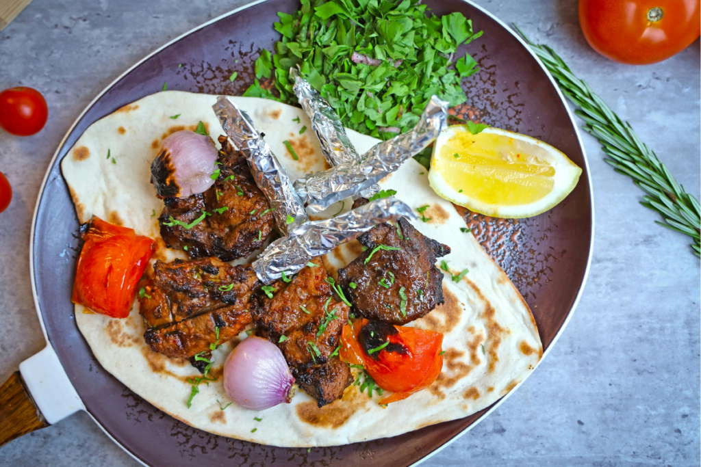 Image of a dinner plate featuring grilled beef slices topped with herbs, a side salad of mixed greens, and a lemon wedge.